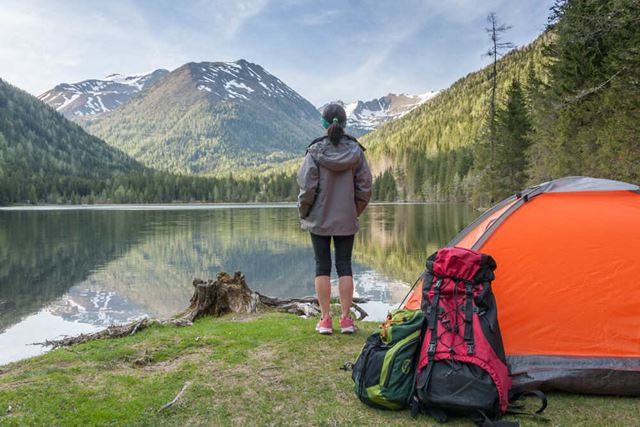 Woman looking over a lake with camping gear behind her